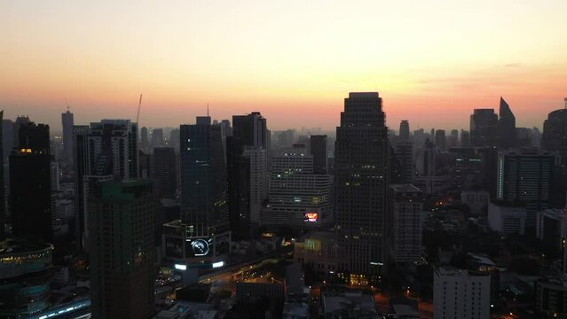 Drone descending above skyline and skyscrapers of Sukhumvit district during colorful red sunrise in Bangkok, Thailand.