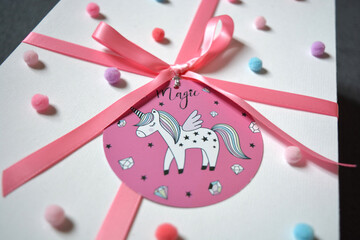 gift box with pink ribbon and unicorn tag and pom poms