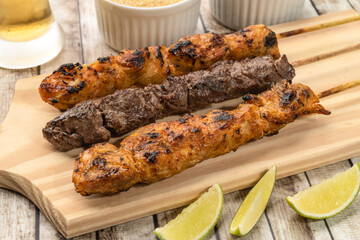 Chicken and meat skewers over wooden board with farofa, lemon and beer