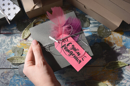 Person Holding A Gray Gift Box With Pink Happy Birthday Tag And With Pink Feathers