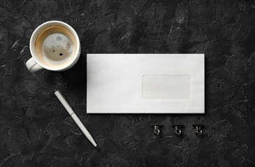 Obraz na płótnie Canvas Blank envelope, coffee cup, pen and clips on black stone background. Blank stationery set. Flat lay.