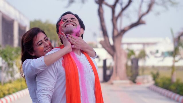 A beautiful Indian lady applying Holi colors (Gulal) on her husband's face - Holi celebration  a cheerful couple  organic colors. A young Indian couple posing together for the camera while embracin...