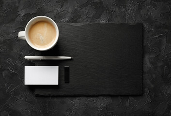 Obraz na płótnie Canvas Blank business card, coffee cup, pen, usb flash drive and slate plate on black stone background. Template for placing your design. Flat lay.