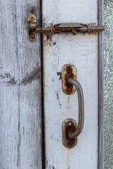Metal latch and doorknob on old wooden door covered with cracked white paint