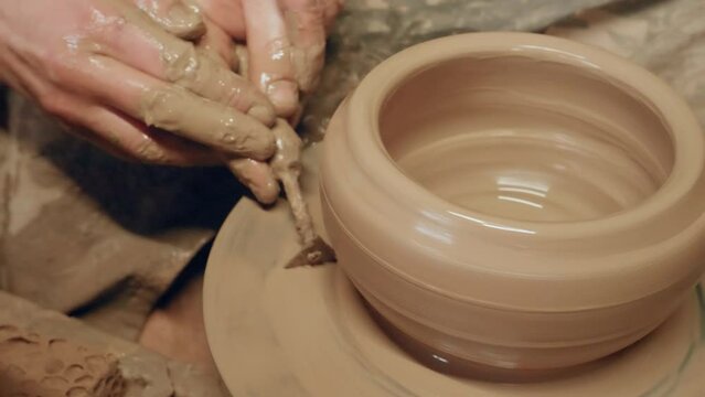 Apprentice scraping off excess clay with triangle knife on ancient revolving pottery wheel