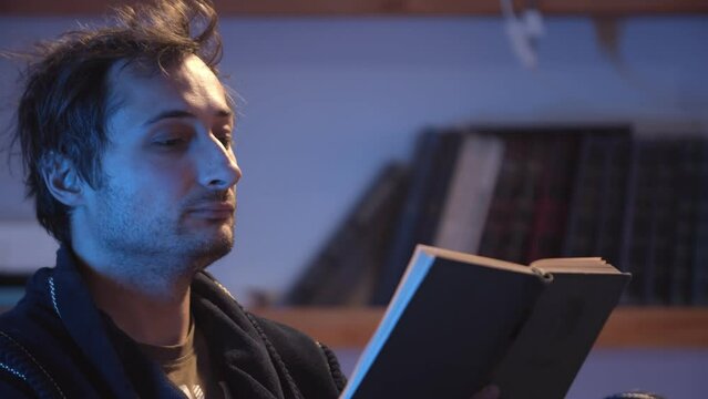 A man in a dressing gown rests in the evening and reads a book at home under a table lamp. Home education and pastime. Close-up