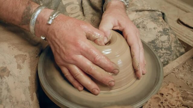 Potter forming hole in chunk of clay on ancient kick operated revolving wheel