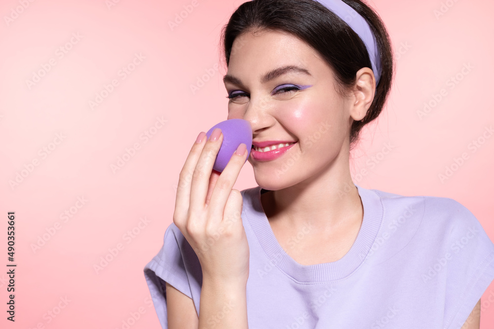 Wall mural playful happy modern girl applying makeup foundation or powder touching nose by lavender make-up bea