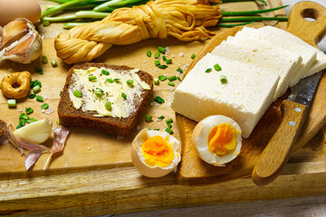 tasty lunch in rural style, healthy food - bread and butter sandwich, feta cheese, eggs, green leek and rye bread, cooked food on a white wooden boards