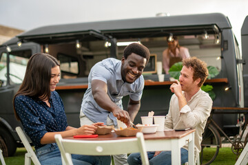 Happy diverse friends eating fast food near truck