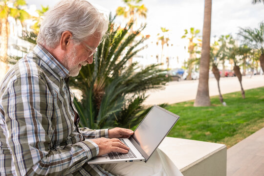Businessman typing on laptop computer sitting in public park. Mature bearded senior man working on digital laptop surfing the net