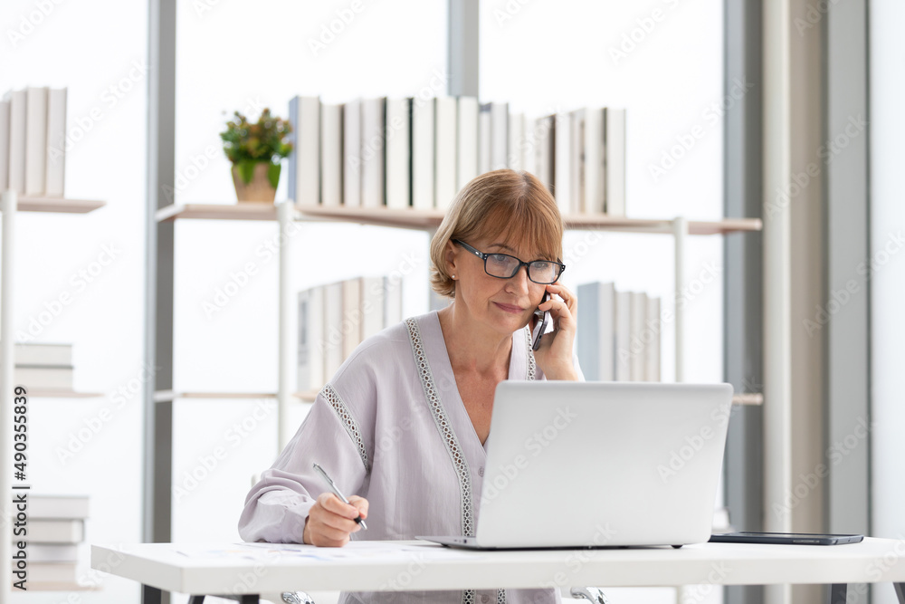 Wall mural senior businesswoman or freelance using laptop computer and talking about work on phone