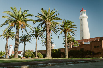 Plaza colonial con palmeras y antiguo faro al fondo en día diáfano