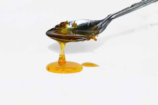 Metal spoon with a pouring drop of golden honey isolated on white background. medicine.