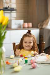 Obraz na płótnie Canvas Joyful little girl paints eggs for Easter holidays. Happy Easter