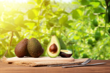 Set of avocados on a wooden table outside with natural background of green leaves - Powered by Adobe