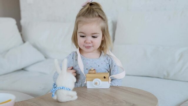 Small adorable girl playing with wooden toy camera and fluffy rabbit toy