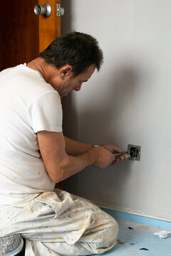 Electrician kneeling on the floor installing a plug socket