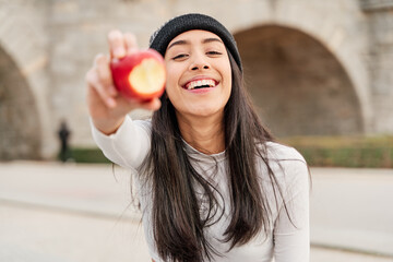 Young and beautiful latin woman holding a bitten apple and showing it to the camera. woman with perfect teeth eating healthily, Healthy life concept