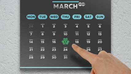 Fototapeta na wymiar Close-up of a male hand pointing finger to Saint Patrick's Day on a black March page of the wall calendar 2022