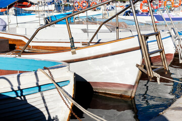 Fototapeta na wymiar Row of many small old wooden vintage colorful bright fishing ships moored at fisherman village marina clear water bay on bright sunny day. Sea harbor with traditional retro vessels background