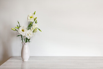 White flowers Eustoma or Lisianthus in vase on light wooden background with copy space