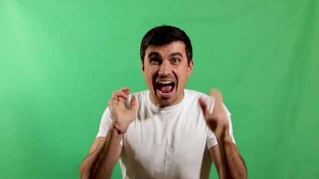 A handsome young man in a white shirt expresses ecstatic joy with a smiling face and shaking hands. Green screen