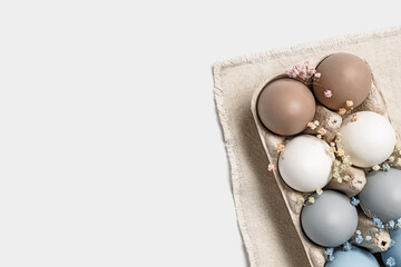 Easter eggs pastel colored in egg box decorated small flowers. Minimal Easter celebration concept, dyed chicken egg with color gradient from blue to beige coloured in carton pack. Top view