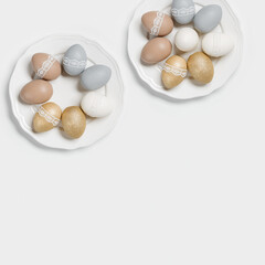 Painted Easter eggs golden, gray, beige colored on white plate, light background. Chicken egg pastel shades with tape lace decor. Easter holiday food, minimal design aesthetic flat lay