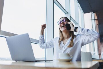 A young female manager in glasses works at a laptop and gesticulates emotionally with her hands...
