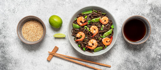 Fototapeta na wymiar Stir fry buckwheat soba noodles with shrimps and vegetables in a bowl. Gray concrete grunge background. Asian traditional food. Top view. Banner