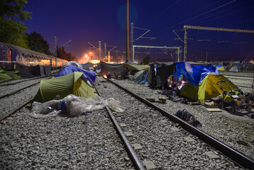 Long exposure of improvised tent city on railway tracks at night. Transit refugee/migrant camp at...