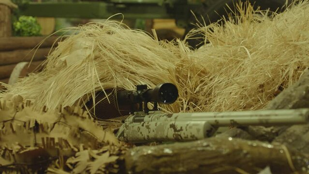 Close up view of sniper dressed in ghillie suit or grass cloak waiting and looking by rifle optics . Sharpshooter aims and shoots . Sharp shooter shooting . Shot on ARRI movie camera in Slow Motion
