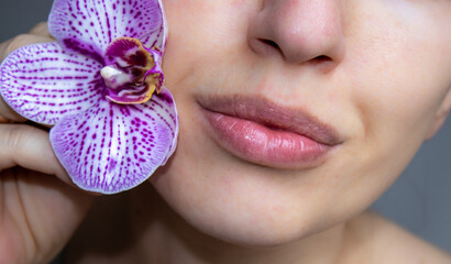 pretty woman with purple orchid flower in the mouth or next to the face. no eyes visible, close up....