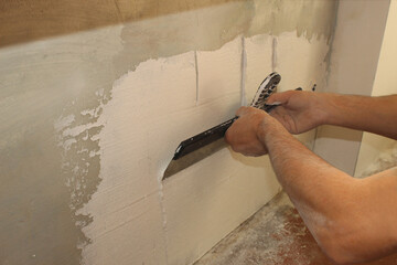 Close-up of a professional builder's hands applying fresh plaster to a wall. Internal finishing...