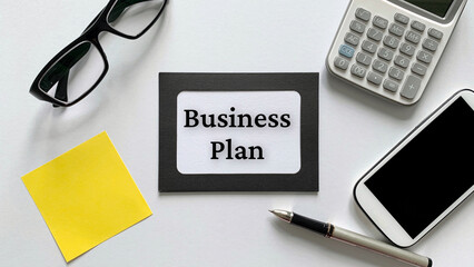 Business plan text on notepad with glasses, calculator, phone and yellow sticky note background. Business concept.