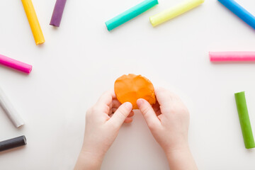 Baby hands holding and kneading modeling clay on white table background. Closeup. Point of view shot. Toddler development. Preparing material for making different colorful shapes. Top down view. © fotoduets