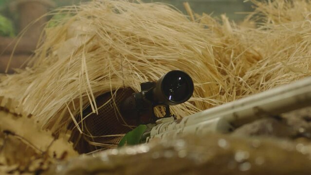 Close up view of sniper dressed in ghillie suit or grass cloak waiting and looking by rifle optics . Sharpshooter aims and shoots . Sharp shooter shooting . Shot on ARRI movie camera in Slow Motion 