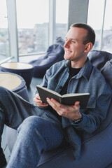 A male businessman in a casual suit resting in a comfortable pouf while working, an attractive freelancer in a suit works remotely and checks notes in a notebook