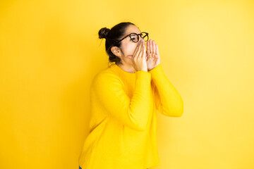 Young beautiful woman wearing casual sweater over isolated yellow background shouting and screaming loud to side with hands on mouth