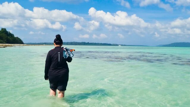 Indian woman in scuba suit walking away with snorkeling mask tube and fins enjoying this leisure sport in the blue green waters of radha nagar beach in havelock andaman and nicobar island India