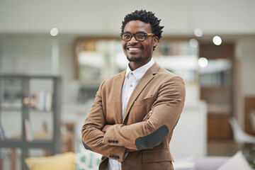 Fototapeta premium Looking sharp and feeling great. Cropped portrait of a confident young businessman standing with his arms folded in his office.