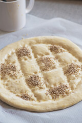 Round dough on a table, preparing ramadan pide with sesame seeds.