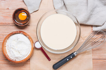 Raw batter with whisk and ingredients on wooden background