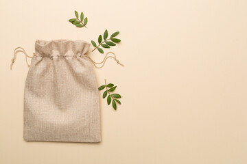 Burlap eco sack with green leaves on color background, top view