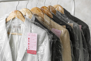 Rack with clean jackets in plastic bags on grunge background, closeup