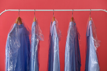 Rack with clean blue shirts in plastic bags on pink background