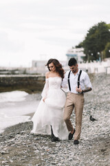 The bride and groom in wedding dresses hug and walk together along the sea in nature on an outdoor trip. Husband and wife in love spend their honeymoon. Selective focus