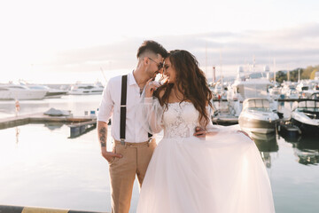 Happy lovers, the bride and groom in elegant wedding dresses go on a honeymoon by sea on  yacht in...