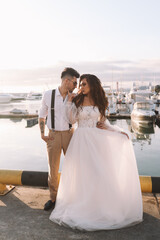 Happy lovers, the bride and groom in elegant wedding dresses go on a honeymoon by sea on  yacht in the marina in Sochi in summer outdoor. Off-site chamber wedding ceremony for a married couple in love